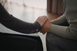 One person's hand reaches out to another's clasped hands in support. 