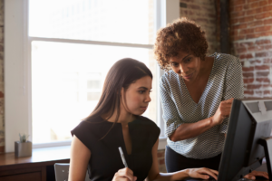 Teacher looks over adult student's shoulder as she looks at a computer screen