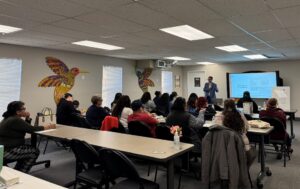 Adults sit in rows in a classroom looking at a presentation at the front of the room